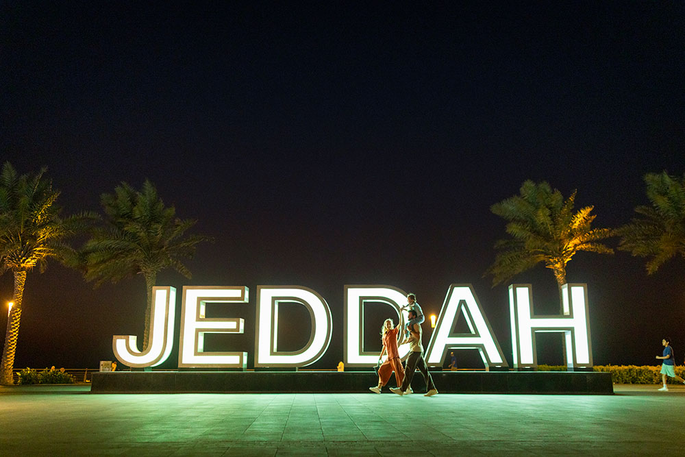 Famille se promenant devant le panneau « Jeddah » de nuit